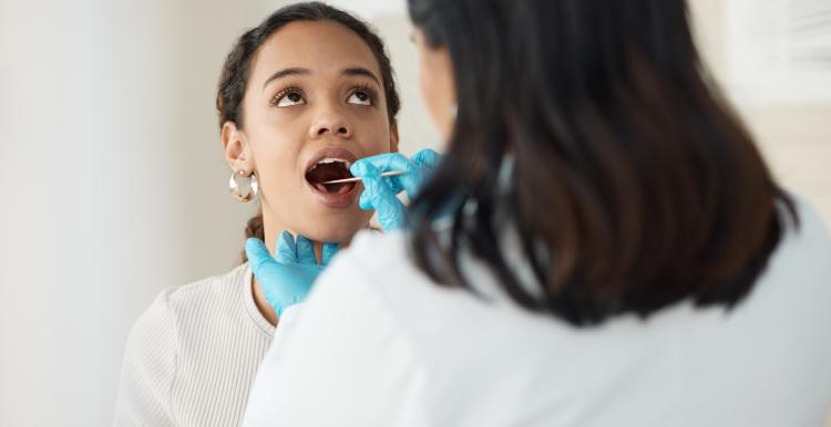 Women with her mouth open whilst a dentist holds an implement in her mouth and looks in her mouth
