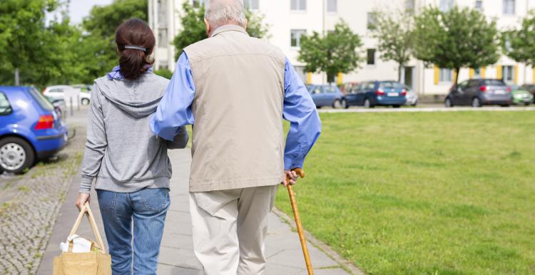 Elderly man walking through a park with his carer