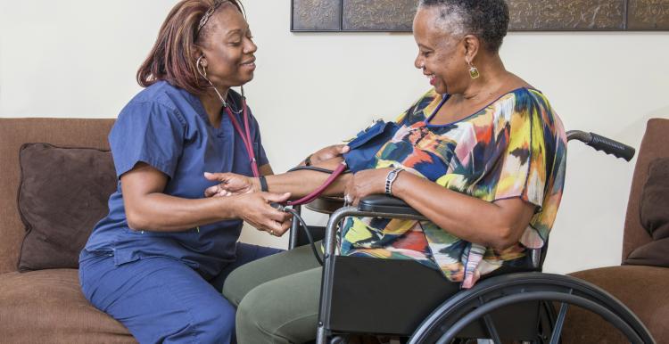 A nurse taking the blood pressure of a woman in a wheelchair