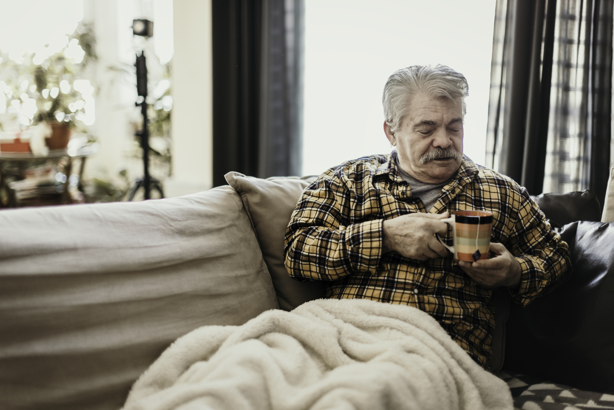 Older man sitting on sofa wrapped in a warm blanket 
