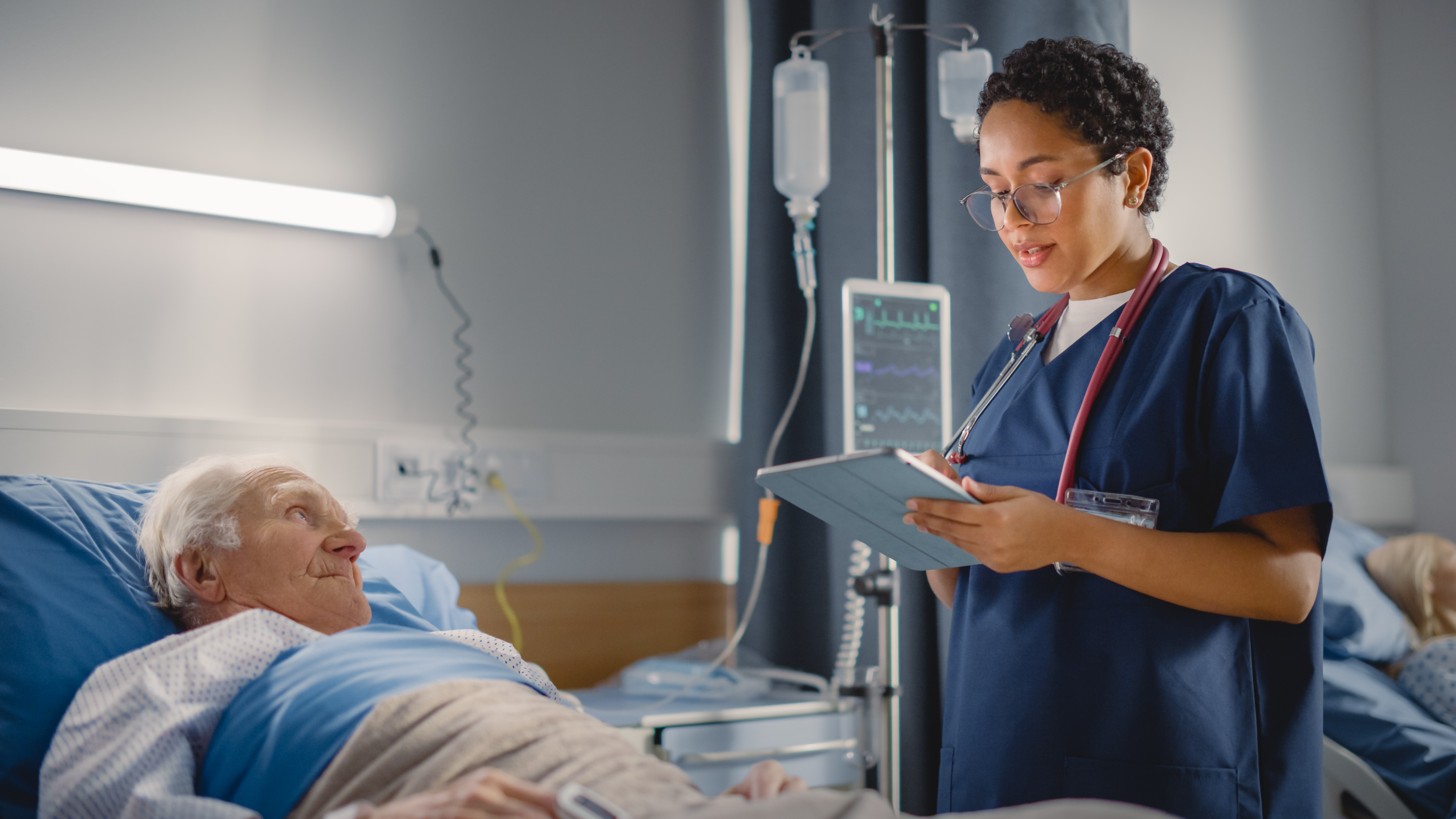 Friendly Head Nurse Talks with Elderly Patient Resting in Bed.