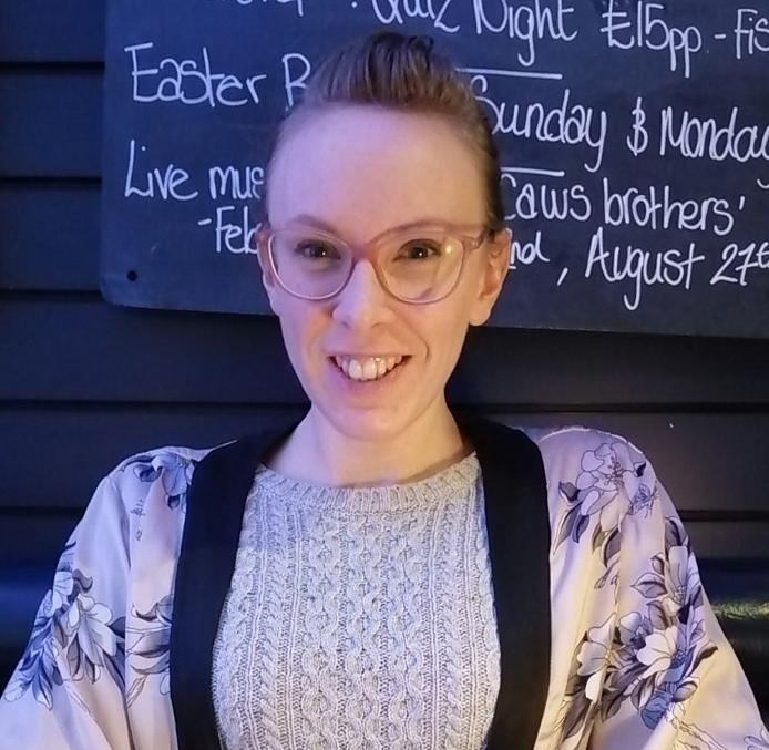 A white woman with a pony tail wearing glasses and smiling at the camera