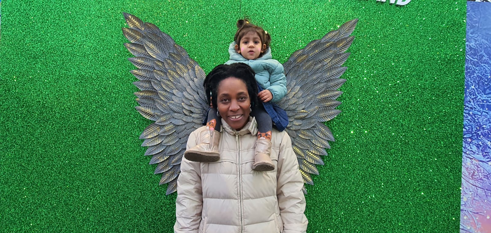 A black woman with a toddler waring a white winter jacket and standing against a green background 