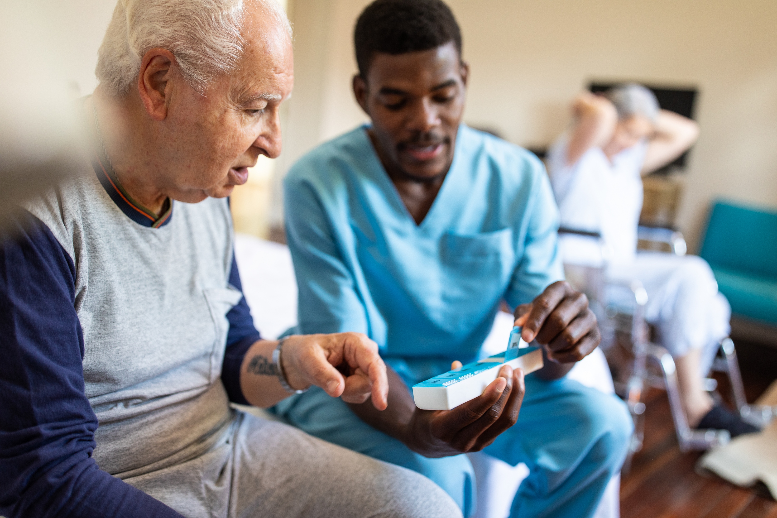 Black male nurse sitting on bed and giving instructions to senior patient when to take his pills in nursing home