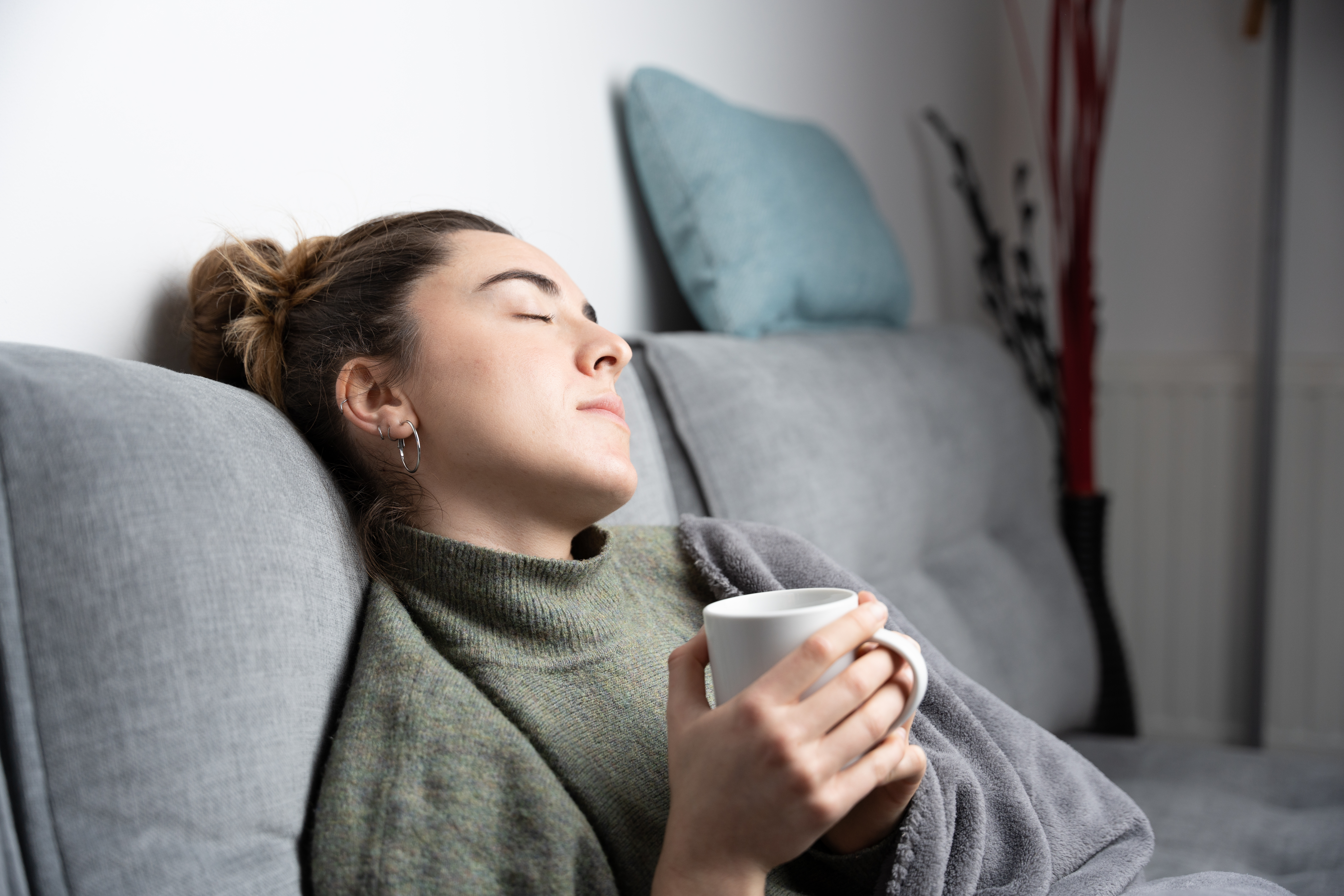 A young tired white woman resting on couch and holding a cup of coffee