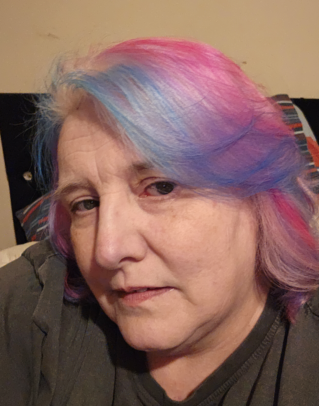 Tanya is tilting her head while looking at the camera. She is a white woman with dark eyes and her hair is dyed pink and blue.