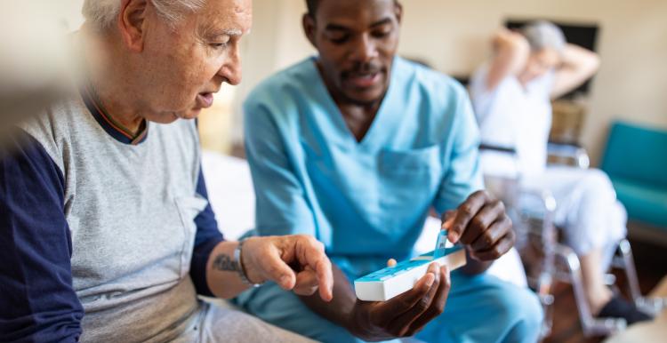 Black male nurse sitting on bed and giving instructions to senior patient when to take his pills in nursing home