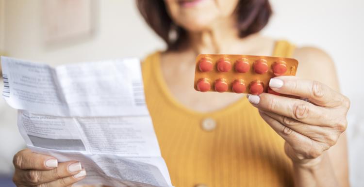 Middle aged lady wearing a yellow top looks at prescription and medication.
