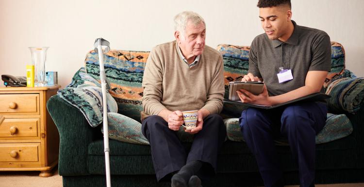 A senior man sitting with a care worker at home talking through treatment plan