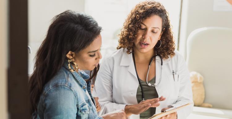 A female doctor discusses a young patient's diagnosis with the patient's mother. They are reviewing the patient's test results. Both are women of colour.