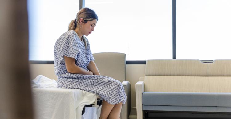 he anxious, sad, young female patient wears her gown as she waits in the hospital room.