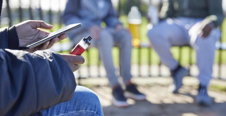 Close Up Of Teenagers With Mobile Phone Vaping in a park