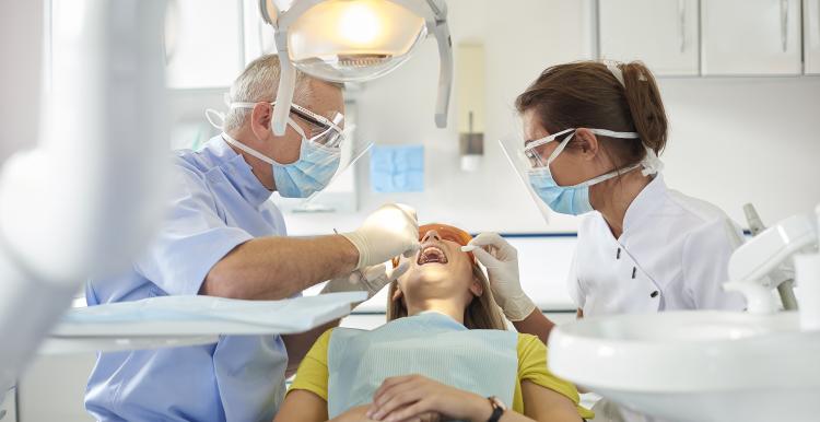 A dentist and dental nurse sit either side of a young woman as they carry out an exam in a bright surgery space
