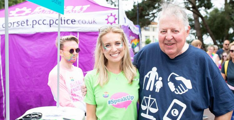 Older man with his arm round a younger woman at Bournemouth Pride. They are both smiling.