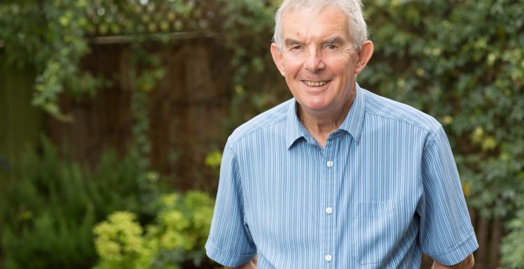 An older man in a blue shirt standing in a garden