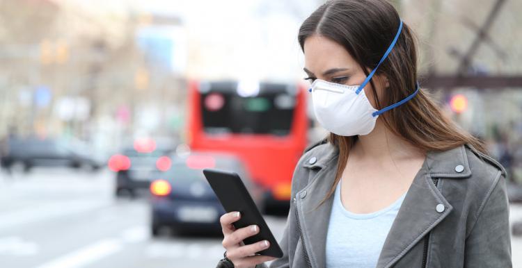 Woman with protective mask using smart phone with city traffic background