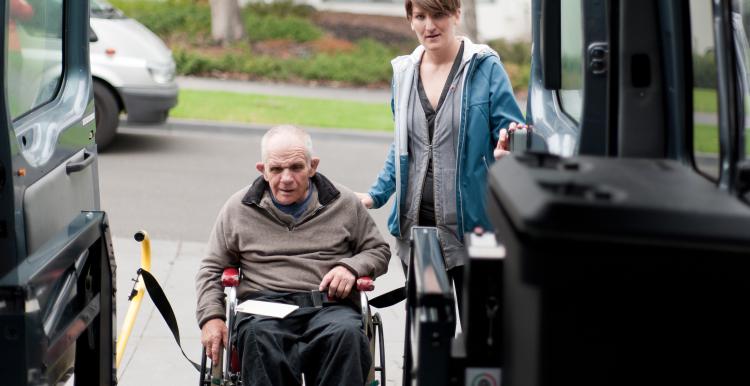 Man in wheelchair being helped into a minibus