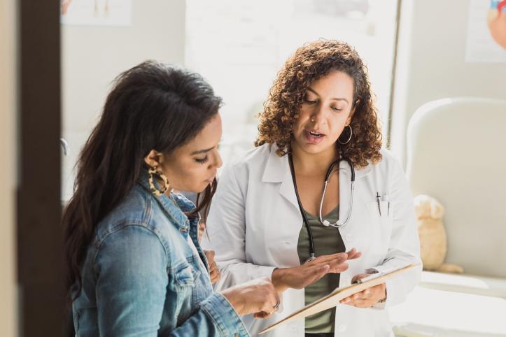 A female doctor discusses a young patient's diagnosis with the patient's mother. They are reviewing the patient's test results. Both are women of colour.
