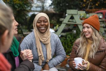 A diverse group of women sit outdoors wearing warm casual clothing on a sunny cold winters day