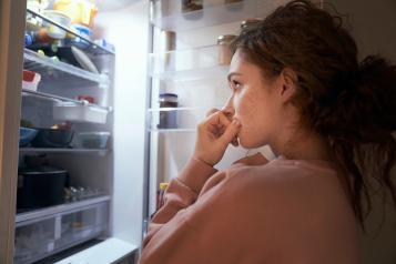 A young woman with a worried expression looks into a fridge filled with food