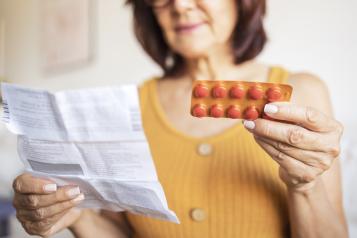 Middle aged lady wearing a yellow top looks at prescription and medication.