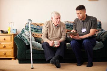 A senior man sitting with a care worker at home talking through treatment plan