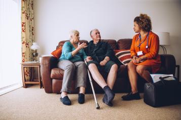 Elderly couple talking to their healthcare worker at home. They are sitting on the sofa in the living room.