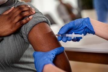 A close of of a black persons arm as hands wearing blue latex gloves give them an injection