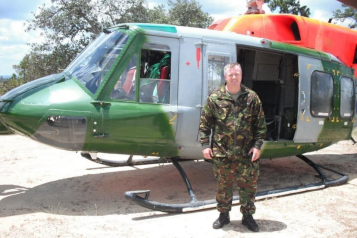 Shaun is wearing a camouflage uniform and standing in front of a helicopter.