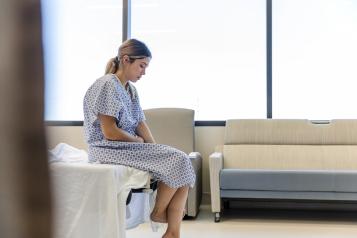 he anxious, sad, young female patient wears her gown as she waits in the hospital room.