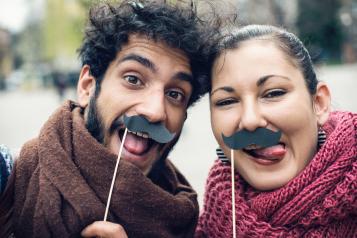 Couple making funny faces and making selfie with fake moustaches for Movember
