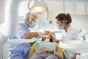 A dentist and dental nurse sit either side of a young woman as they carry out an exam in a bright surgery space