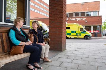 Two older women sitting on a bench outside hospital