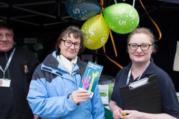 two women at a Healthwatch stand holding leaflets and balloons
