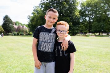 Two boys stood in the park with their arms round each other 
