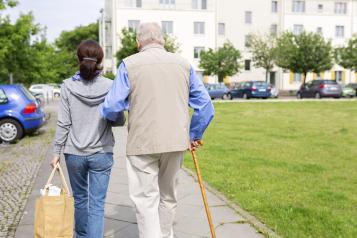 Elderly man walking through a park with his carer