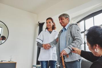 female nurse helping an elderly gentleman walk down a corridor