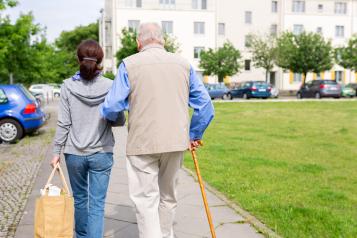 A carer supporting an elderly man with a walking stick