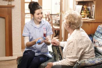 A nurse speaking to an elderly person on the sofa